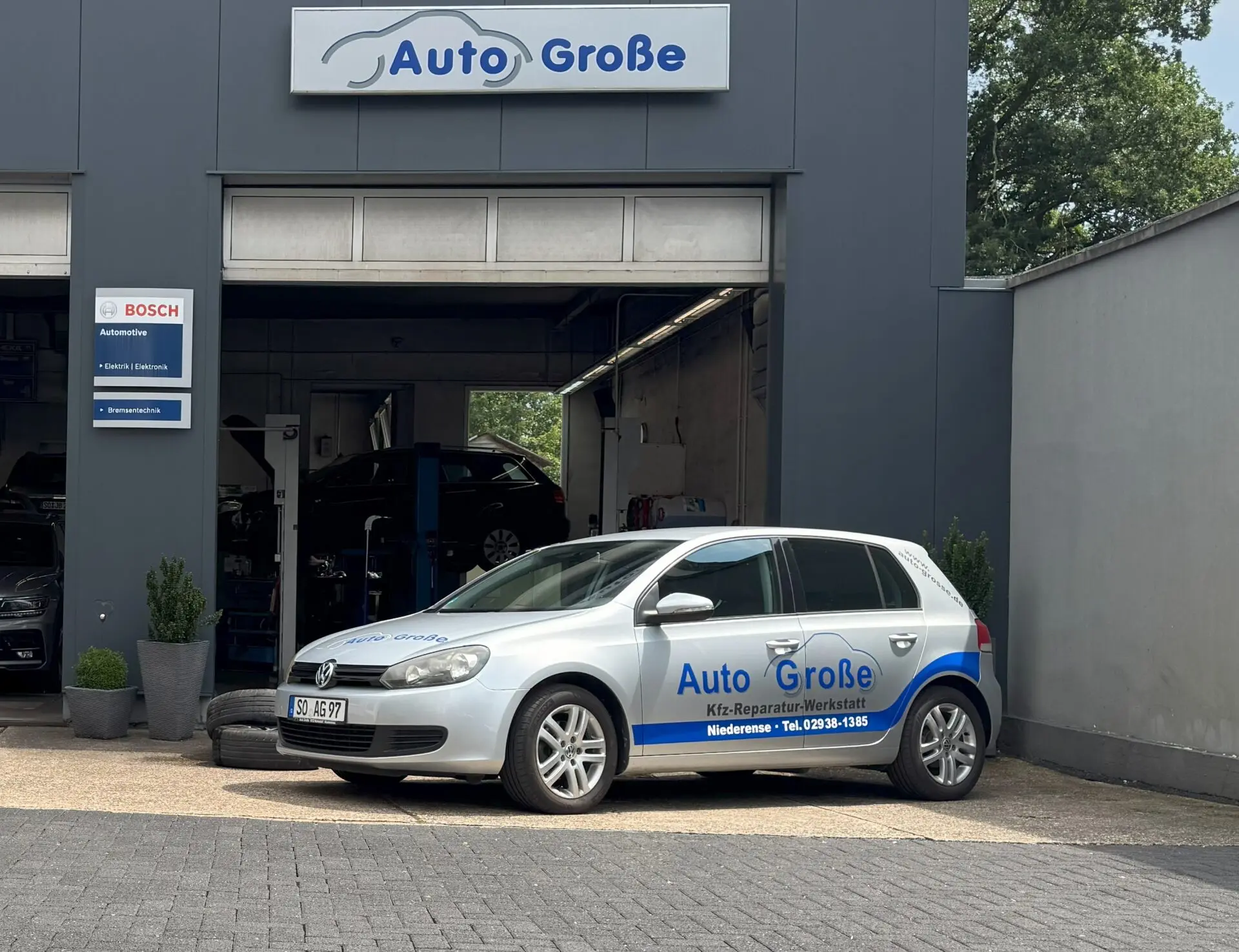 Ein grauer Volkswagen Golf vor der Kfz-Reparatur-Werkstatt Auto Große mit offenen Garagentoren.