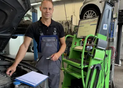 Mechaniker steht in einer Werkstatt neben einem Auto auf einer Hebebühne.